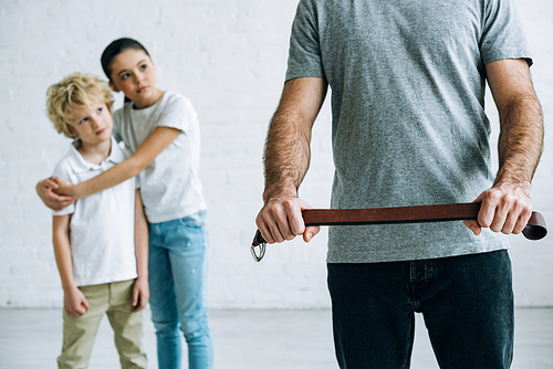 partial view of abusive father with belt and embracing kids at home