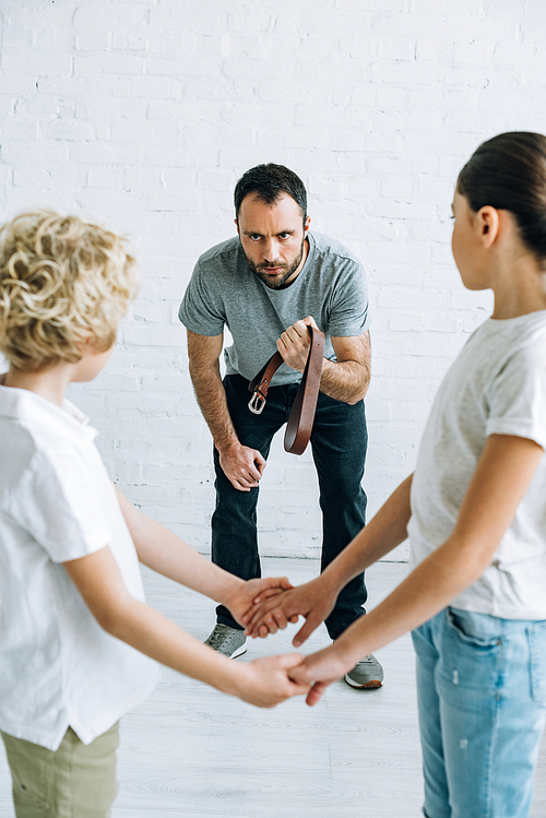 abusive father holding belt and children holding hands at home