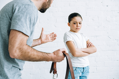 partial view of father holding belt and scolding upset daughter at home