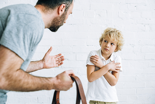 cropped view of father holding belt and scolding son at home