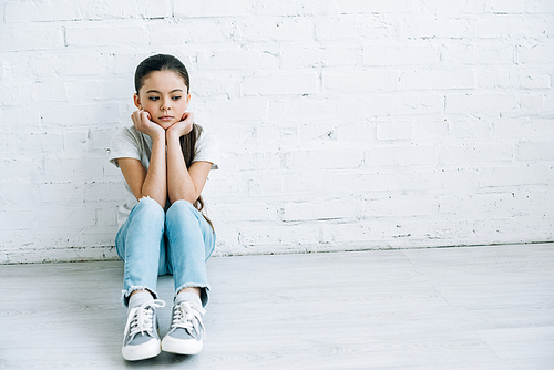 upset preteen child sitting on floor at home