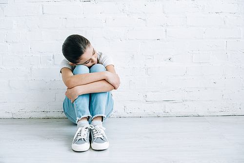 upset preteen child sitting on floor at home