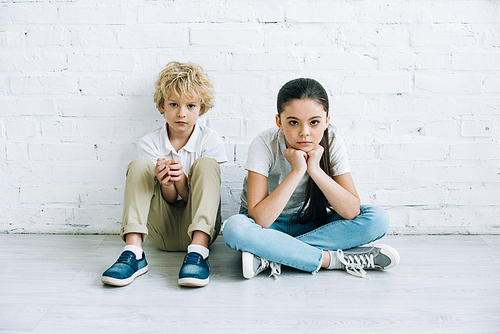 upset sister and brother sitting on floor at home