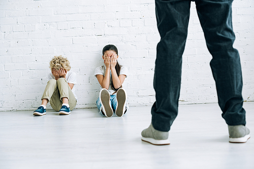 cropped view of abusive father holding belt and scared kids sitting on floor