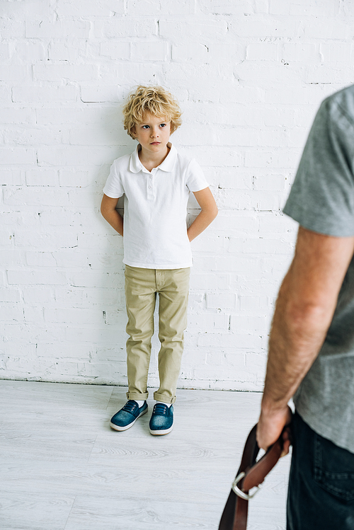 cropped view of father holding belt and son having conflict