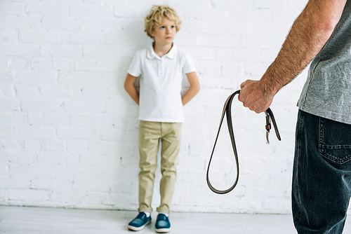 cropped view of father holding belt and son having conflict
