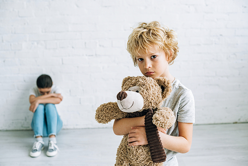 preteen boy holding teddy bear while his sister crying at home