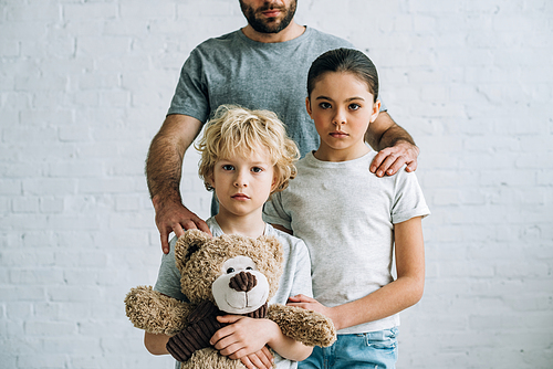partial view of father and kids with teddy bear at home