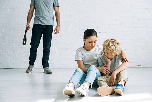 partial view of abusive father and sad kids sitting on floor