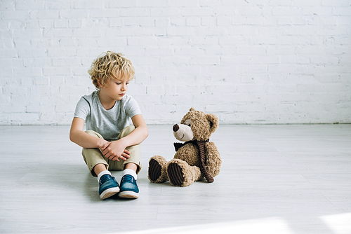 sad preteen boy with teddy bear sitting on floor