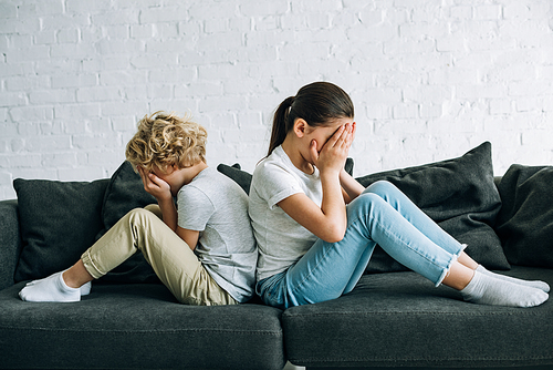 two sad kids sitting on sofa in living room