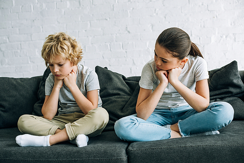 two sad kids sitting on sofa in living room