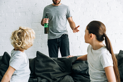 cropped view of alcohol addicted father with beer and upset children on sofa