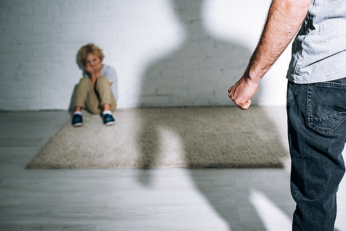 partial view of abusive father and scared son sitting on carpet