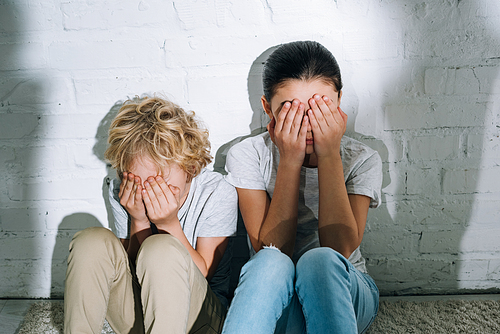 scared children covering eyes with hands while sitting on carpet