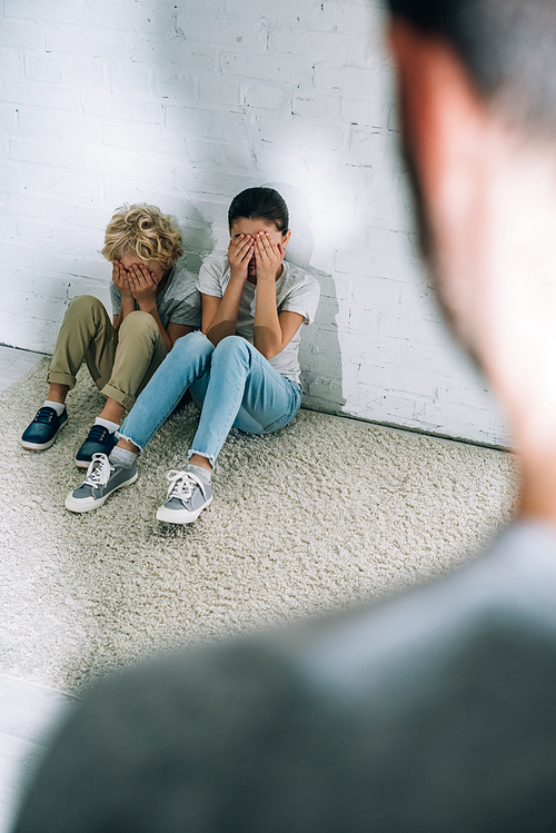 cropped view of father and scared children sitting on carpet