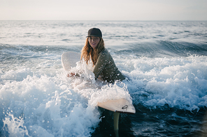 young woman in wetsuit with surfboard going into ocean in evening