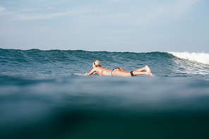 young woman in bikini swimming on surfboard