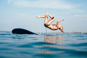 side view of woman falling off surfboard into water
