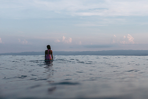 silhouette of female surfer sitting on surfboard in water
