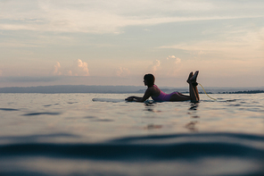 silhouette of girl lying on surfboard in water in ocean at