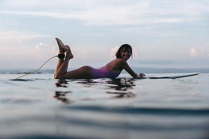 smiling surfer lying on surfboard in water in ocean at sunset