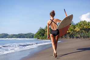 back view of young surfer walking with surfboard on beach