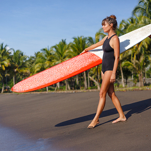 beautiful young girl in black swimsuit holding surfboard on beach