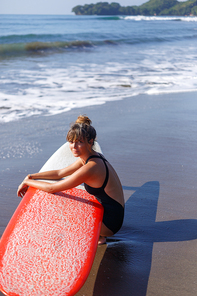 attractive surfer in swimsuit sitting with red surfboard near ocean