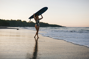 sportswoman in swimming suit with blue surfing board walking on beach