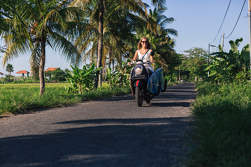 young woman riding scooter with surfing board