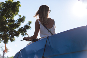 back view of woman riding scooter with surfing board against blue sky