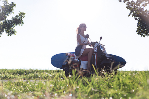 side view of woman riding scooter with surfing board against blue sky