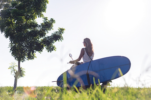 side view of woman riding scooter with surfing board against blue sky