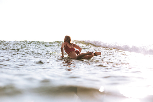 back view of woman in swimming suit surfing in ocean