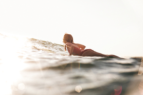 side view of woman in swimming suit surfing in ocean