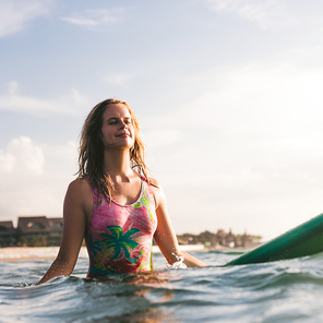 portrait of young woman in swimming suit resting on surfing board in ocean