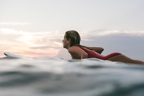 side view of sportswoman in swimming suit surfing alone in ocean