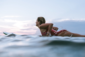 side view of sportswoman in swimming suit surfing alone in ocean