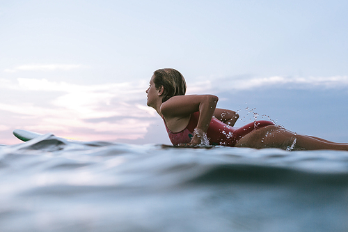 side view of sportswoman in swimming suit surfing alone in ocean
