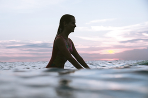 silhouette of woman resting on surfing board in ocean on