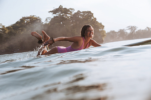side view of smiling sportswoman lying on surfing board in ocean