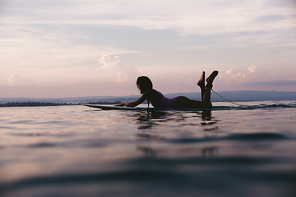 silhouette of sportswoman lying on surfing board in ocean on sunset