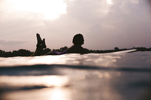silhouette of sportswoman lying on surfing board in ocean on sunset