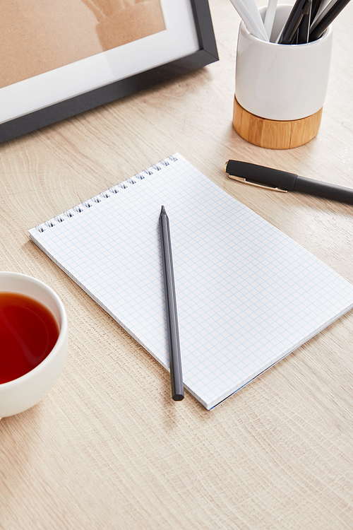 cup of tea and blank notebook with pencil and pen on wooden surface