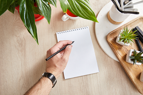 partial view of man writing in notepad near green plants on wooden surface