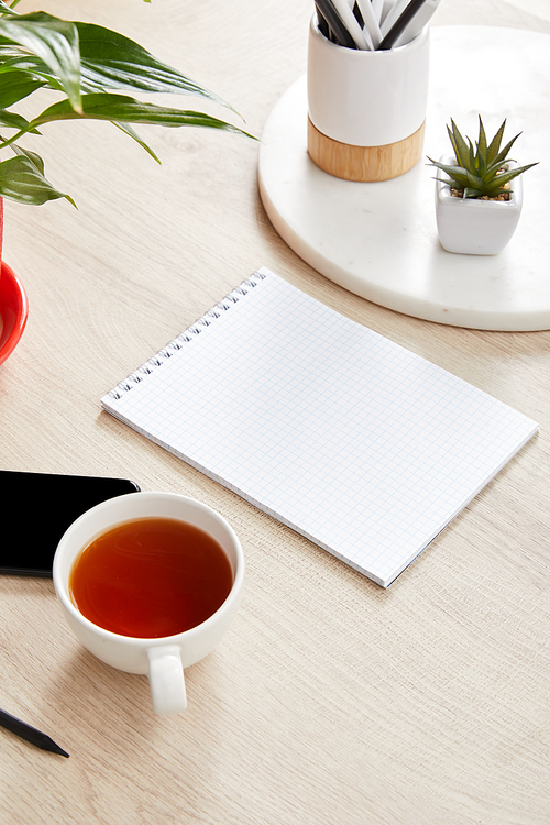 green plants, cup of tea and blank notebook near smartphone on wooden surface