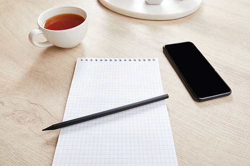 cup of tea and blank notebook with pencil near smartphone on wooden surface