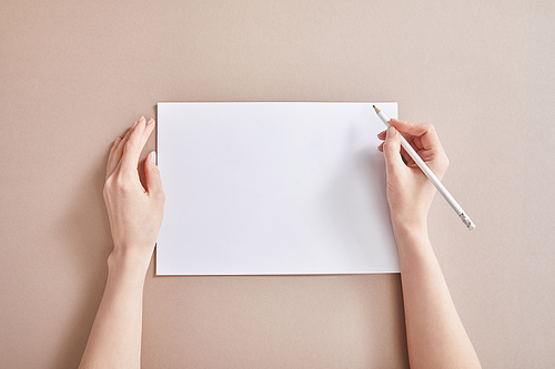cropped view of woman writing on paper with pencil on beige surface