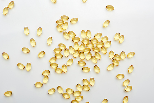 top view of golden fish oil capsules scattered on white background